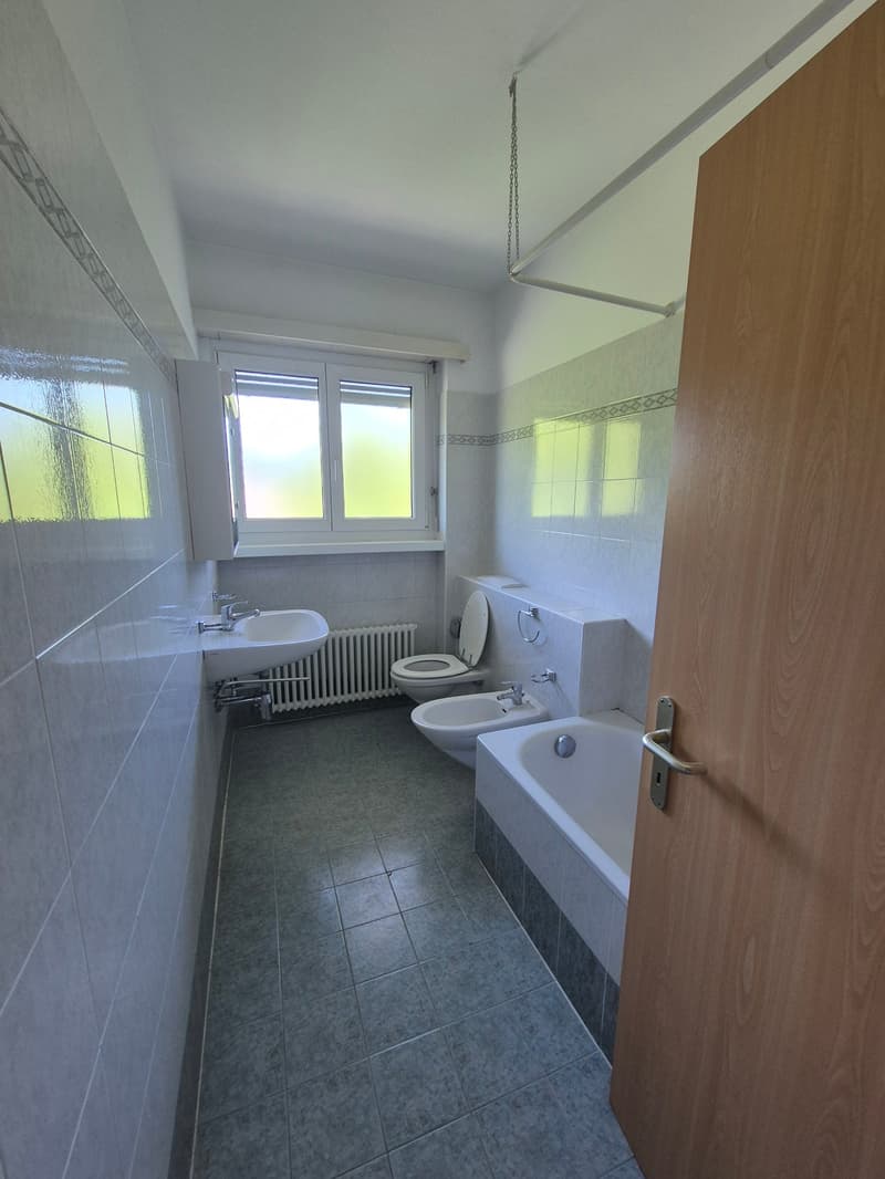 The image shows a bathroom with a tiled floor, a bathtub, a toilet, a sink, and a window. The bathroom appears to be well-lit and has a clean, modern design.