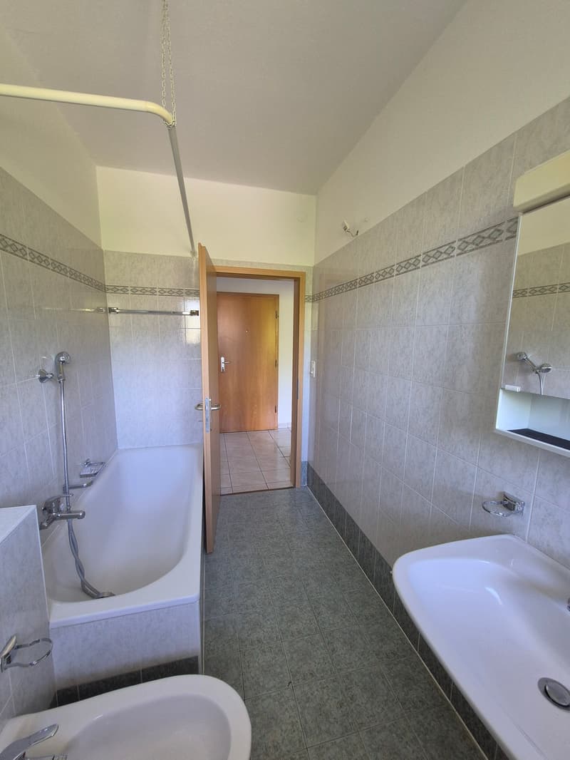 Tiled bathroom with a bathtub, shower, toilet, and a door leading to another room.