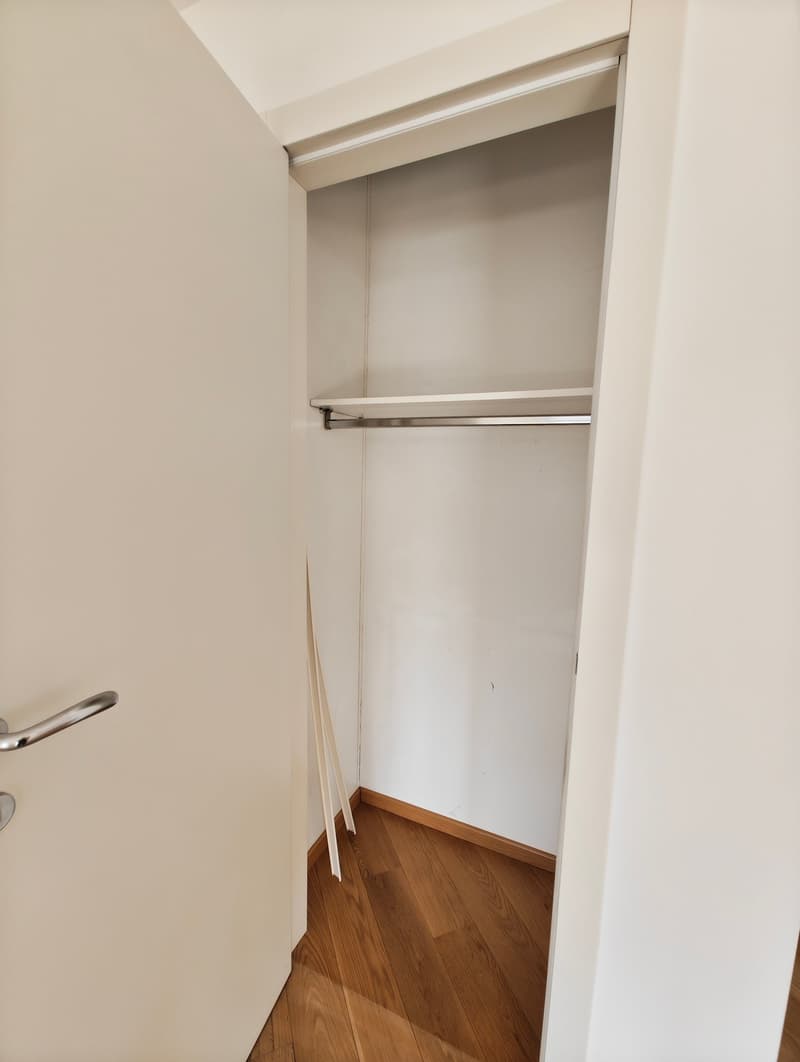 white wardrobe with rod, wooden floor, wooden trim at base of walls