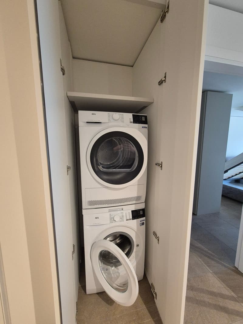 two stacked white washing machines against a wall, white cabinets on either side, tiled floor