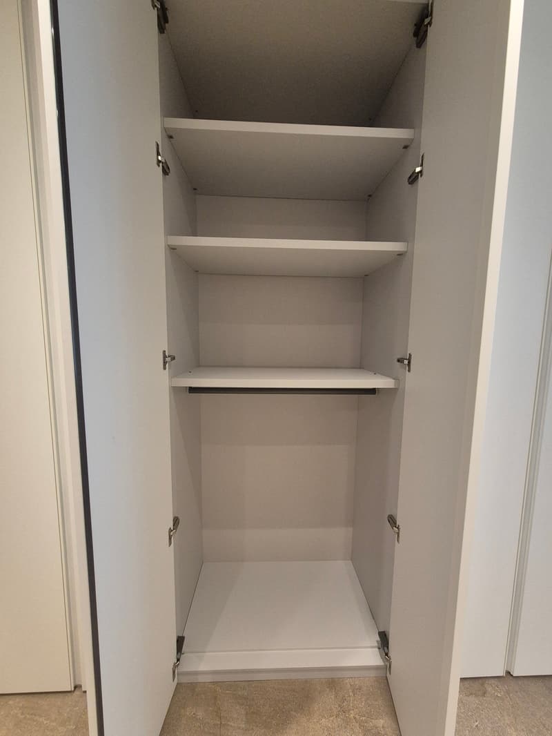 An empty modern white wardrobe with 5 shelves and 2 metal rods.