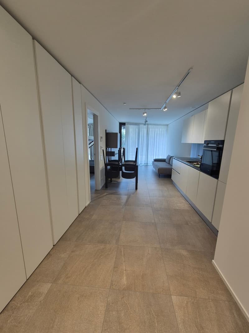 wide hallway, modern kitchen with appliances, dining area with chairs, white cupboards, beige tiles, two doors leading to another room