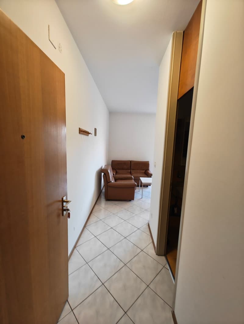 Empty hallway with white tiles, wooden door, white walls, brown leather couch, coffee table