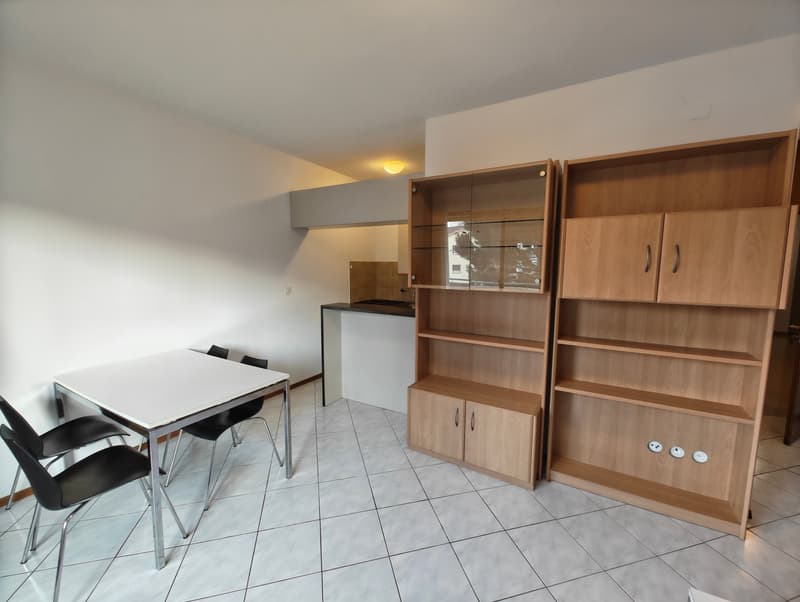 white table, black chairs, wooden shelves, white tiles, kitchen area
