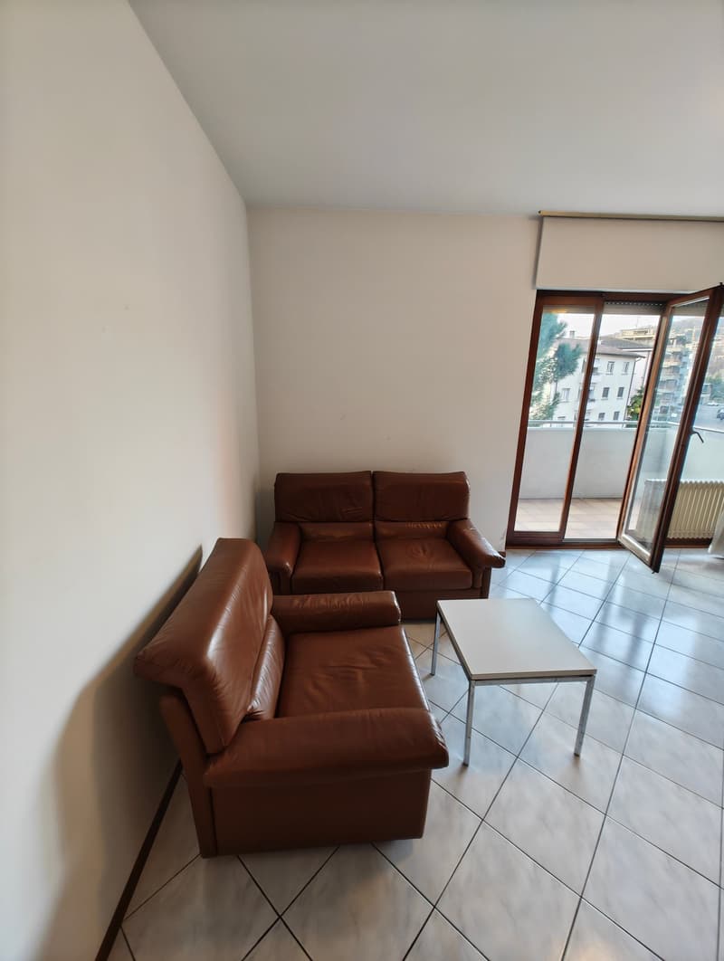 living room with two brown leather sofas, white coffee table, white tiled floor, balcony with glass doors