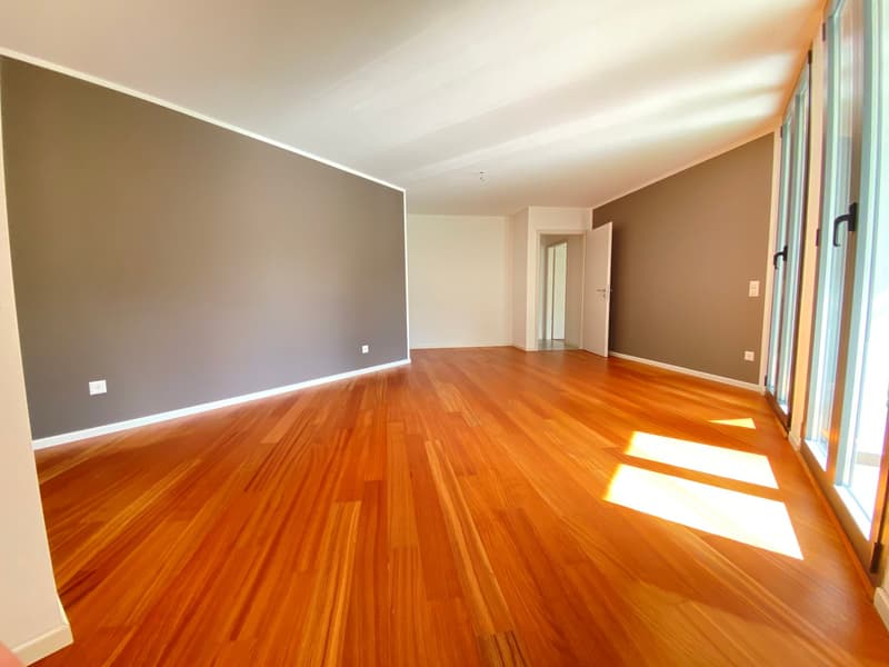 large empty room with hardwood floors, gray walls, glass sliding doors leading to balcony