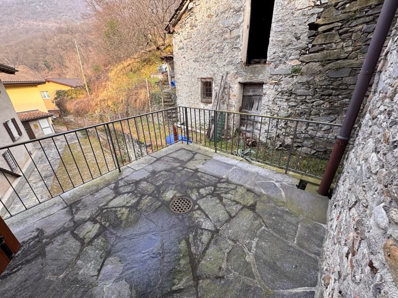 Stone built house, concrete balcony, drain, street on one side, mountains in the background
