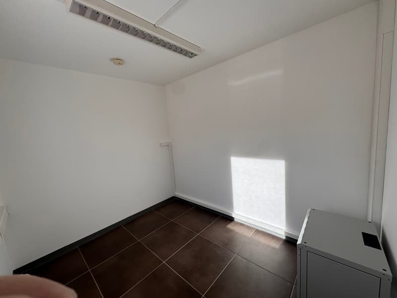 Empty room with white walls, brown tiled floor, and a grey filing cabinet