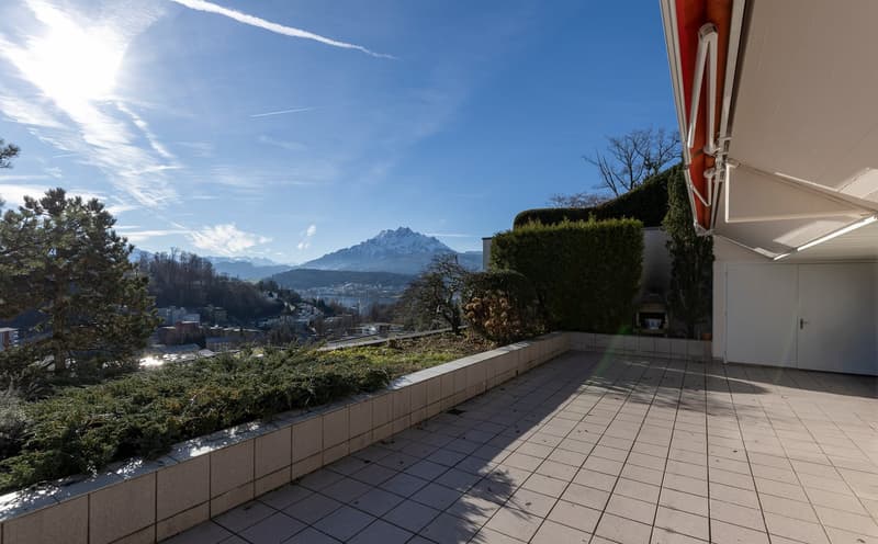Outdoor terrace with tiled flooring, surrounded by greenery and a view of the mountains.