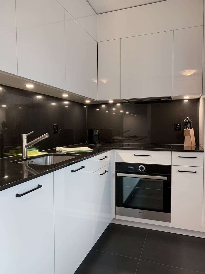 Modern kitchen with white cabinets, black countertops, built-in oven, and dishwasher