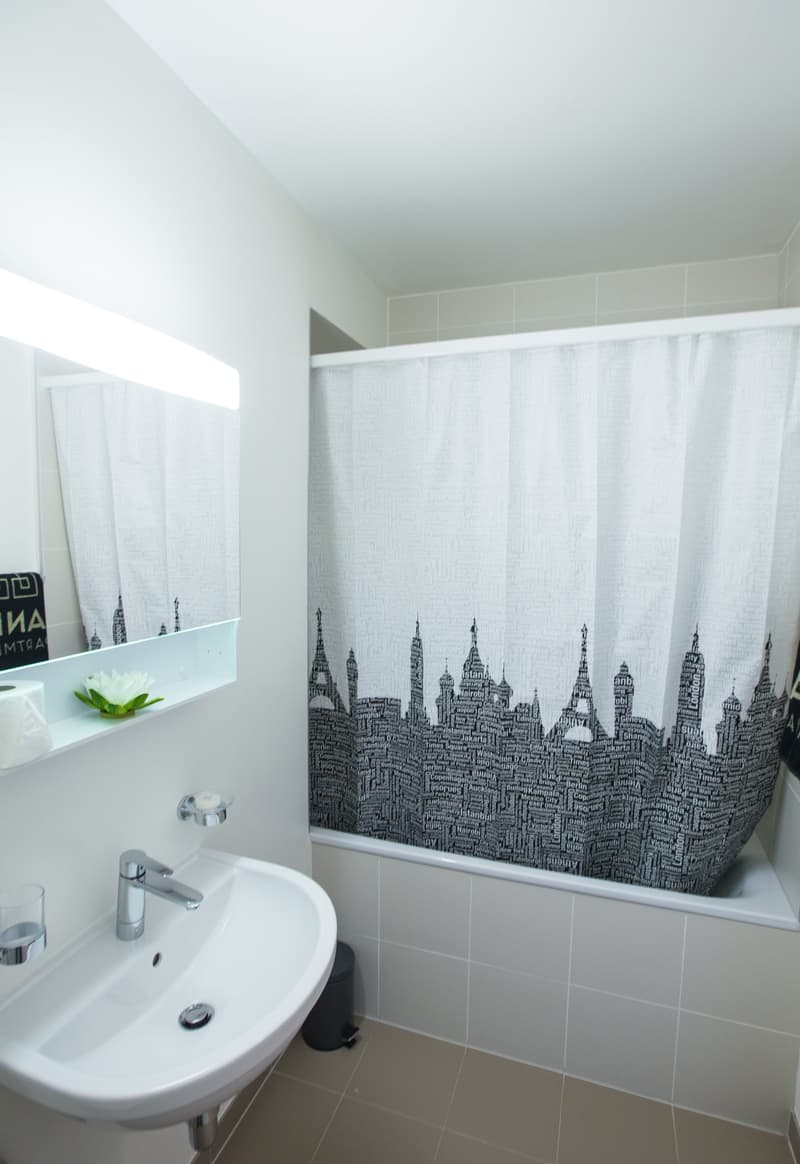 White bathroom with a sink, shower curtain with a cityscape design, and a shelf with a plant