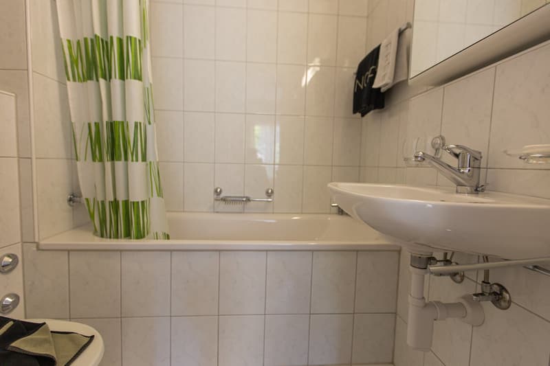 Tiled bathroom with a white sink, shower curtain, and a towel rack