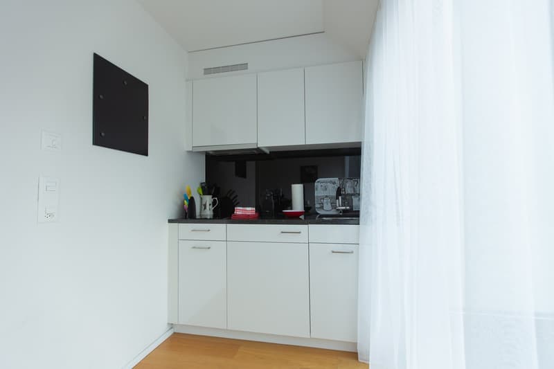 Open concept kitchen with white cabinetry, granite countertops, built-in appliances, wooden floor, black tile backsplash