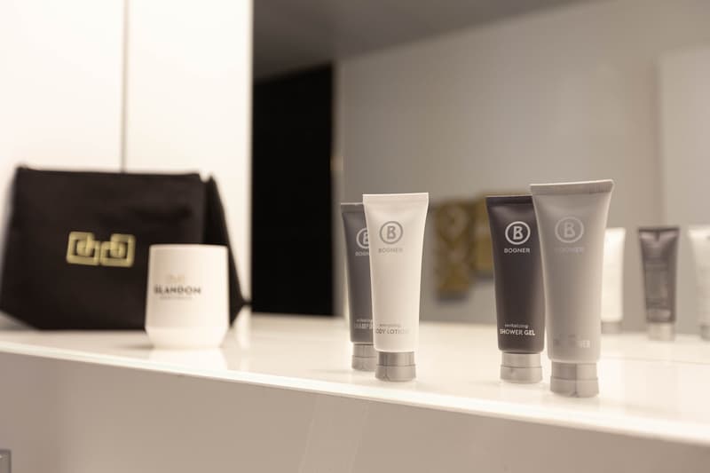 Bathroom amenities including Bogner brand shampoo, body lotion, and shower gel on a shelf, along with a Blandor brand bag