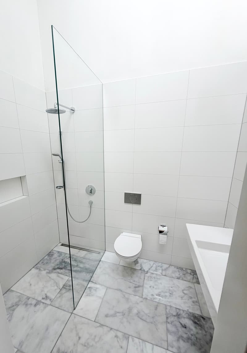 modern bathroom with white tiles, glass shower enclosure, white toilet, white sink, marble flooring