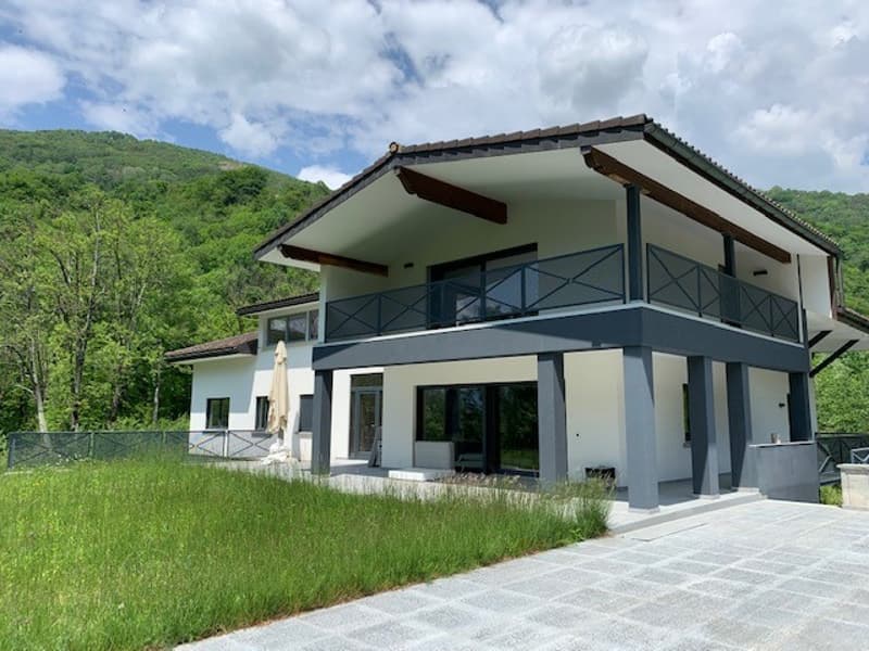 Modern 2 story house, white exterior, grey roof, large windows, balcony, metal railings, patio with umbrella, grassy yard, mountains in background