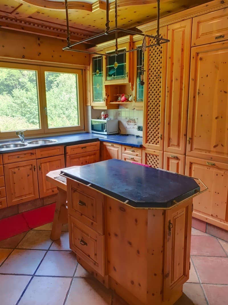 Island kitchen, wood cabinets, blue countertops, island with drawers, kitchen sink with faucet, microwave, window, tiled floor