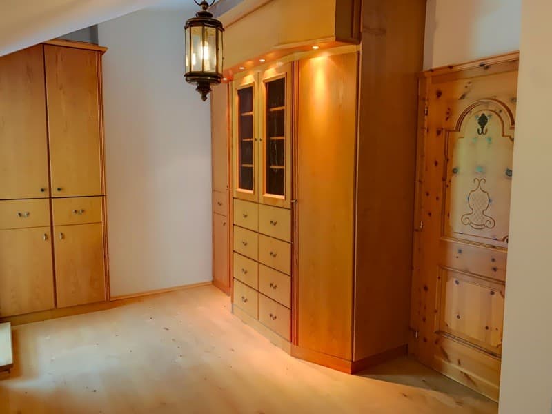 Wooden wardrobes with glass doors and drawers, lamp hanging from ceiling, white walls, wooden floor