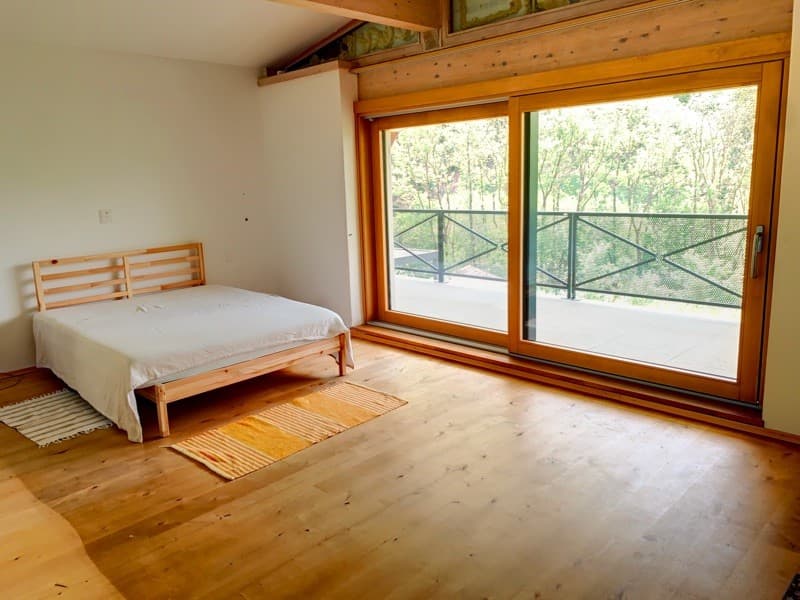 wooden bed, wooden floor, glass sliding door, balcony, wooden railings, trees outside