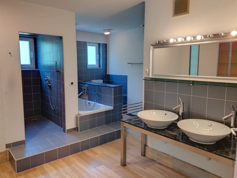 modern bathroom, two sinks, bathtub, shower area, wooden floor, tiled walls, mirror with lights