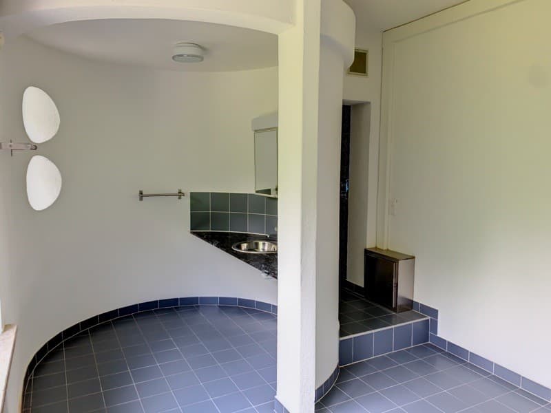 a small room with blue tiles, a silver sink and mirror, and a white ceiling light
