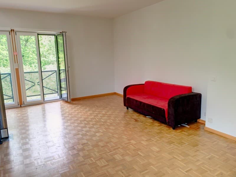 Wooden floor, white walls, large windows, sliding glass doors, red couch, balcony with railing, outdoor view