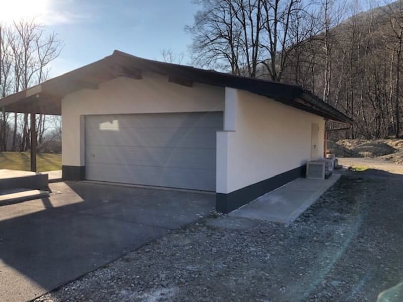 Single-story house, white and gray exterior, attached garage with roll-up door, small canopy above garage entrance, utility box beside garage door, concrete driveway.