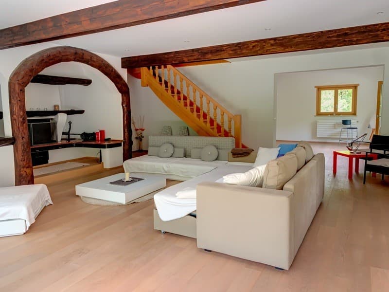 wooden ceiling beams, staircase, floor fireplace, couch, couch with pillows, coffee table, throw pillows, white throw blanket, wooden floor, radiator, window