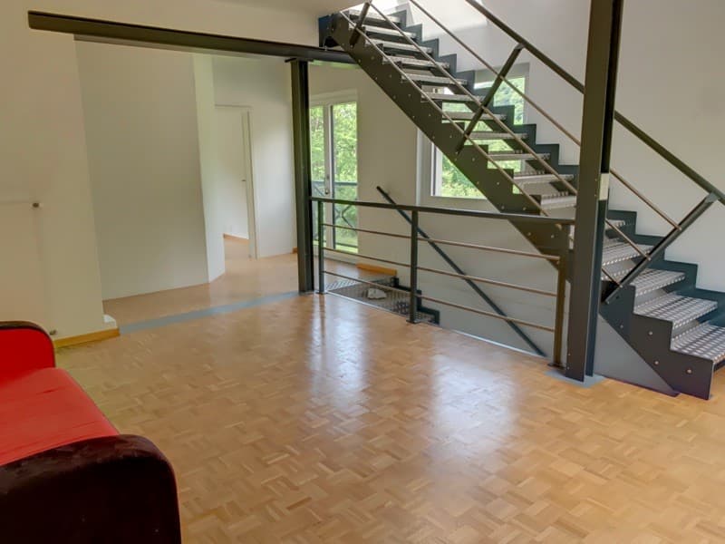 Modern interior with wooden floor, white walls, open sliding door, metal staircase leading to the upper floor, large glass window, red couch