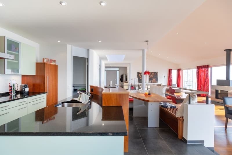 Modern kitchen with granite countertops, wooden cabinets, double sink, wooden island with seating, kitchen appliances, and panoramic windows with red curtains