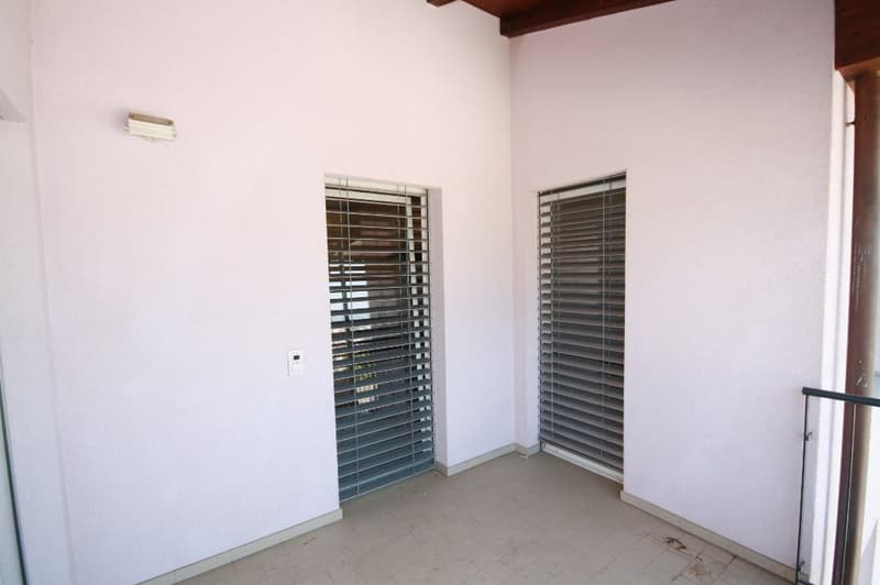 small room, white walls, 2 glass doors with blinds, tiled floor, lamp on the wall