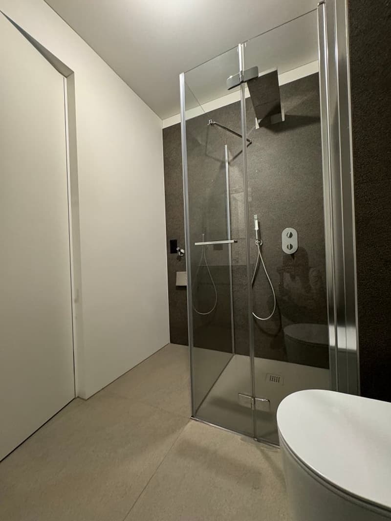 modern bathroom with walk-in shower and glass wall, a toilet and a wall-mounted toilet paper holder, white floor