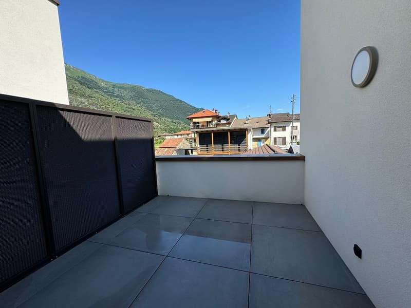Balcony with tiled flooring, overlooking a residential area with buildings and mountains in the background