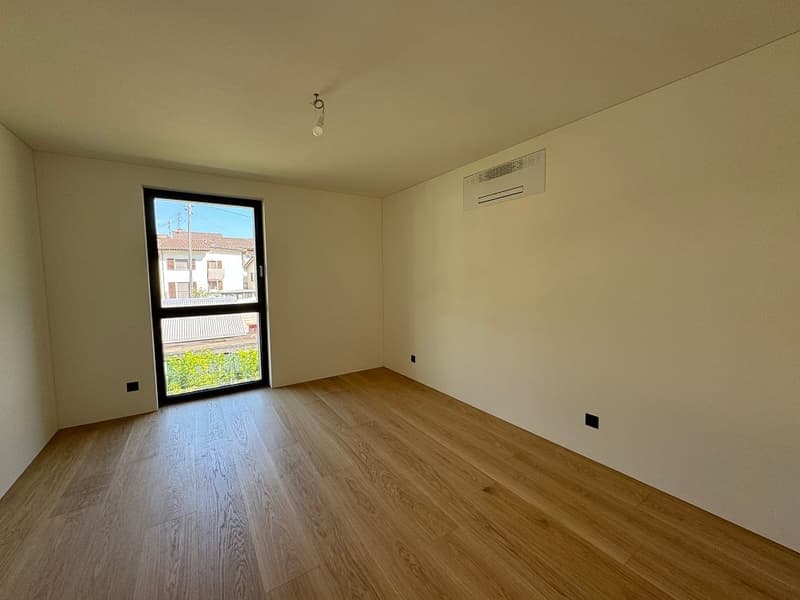 Spacious room with hardwood flooring, white walls, and a large window providing natural light. The room appears to be empty, ready for furnishing and personalization.