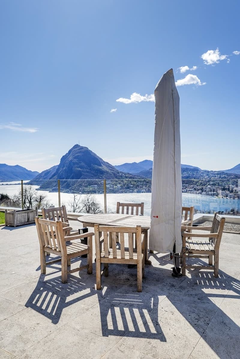 Wooden table and chairs, closed umbrella, tiled floor, view of mountains and lake