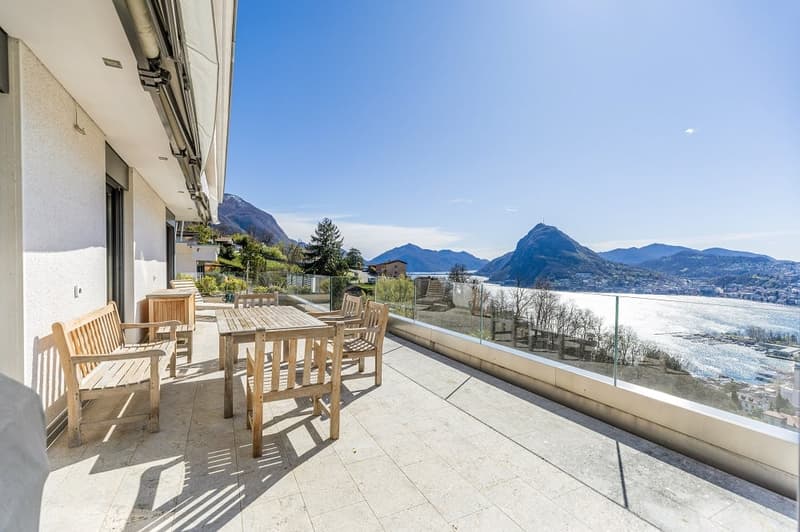 Balcony with wooden furniture, glass railing, tiled floor, view of mountains and water