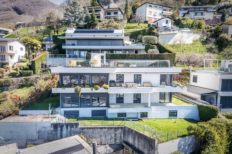 Modern house, white exterior, multiple levels, large windows, multiple balconies, solar panels on the roof, surrounded by greenery