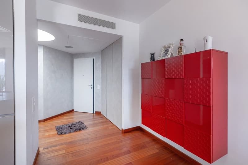wooden floor, white walls, red storage unit, white door, gray rug