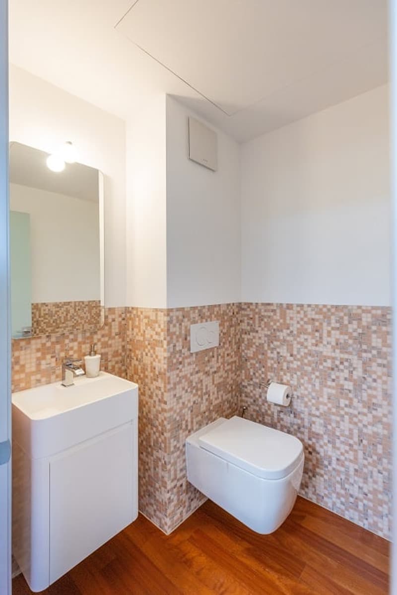 Bathroom with white sink, mirror, toilet, wooden floor, tiled walls