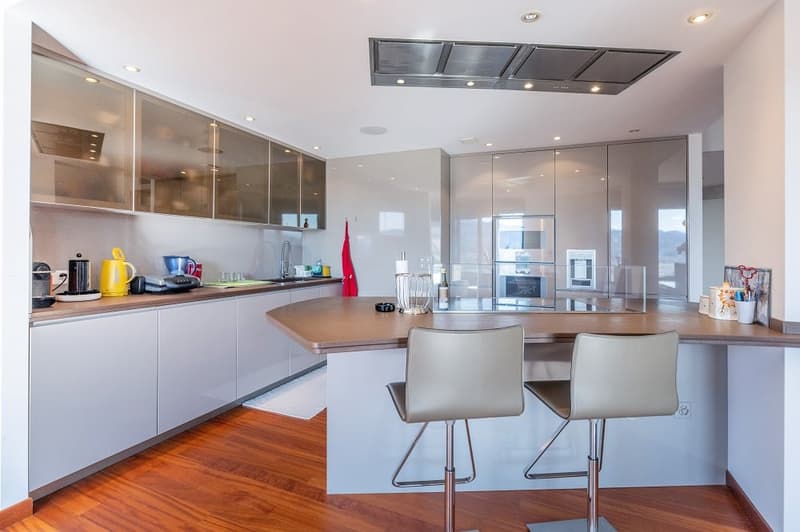 modern kitchen with island, white cabinets, wooden floor, stainless steel appliances, bar stools
