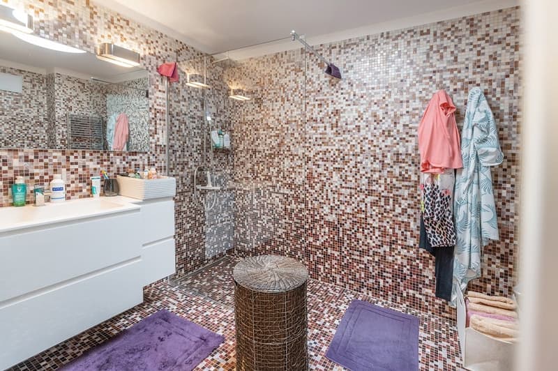 Bathroom with tiled walls, white vanity, shower enclosure, towels, and toiletries