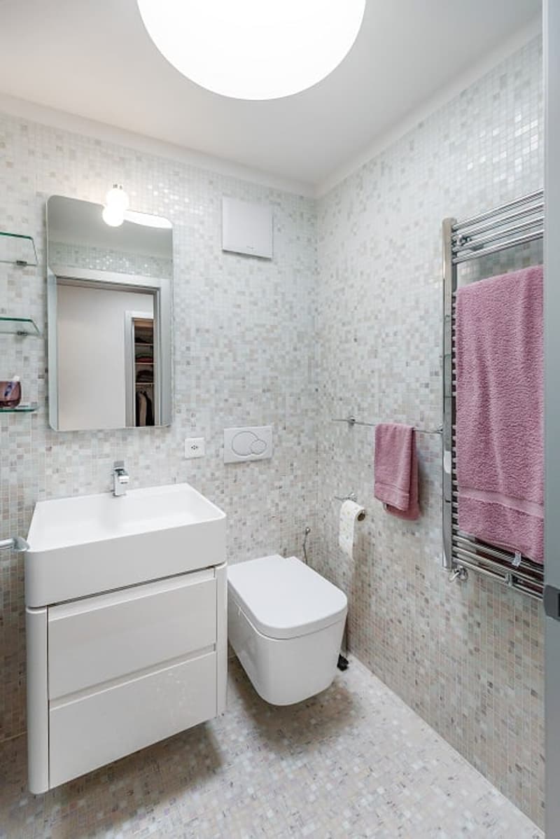 Bathroom with white tiles, white sink, white toilet, mirror, towel rack, and towel