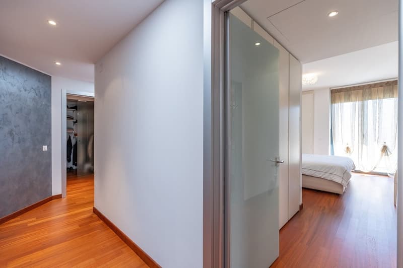 Empty room with wooden floor, white walls, glass door, and a bed in the corner