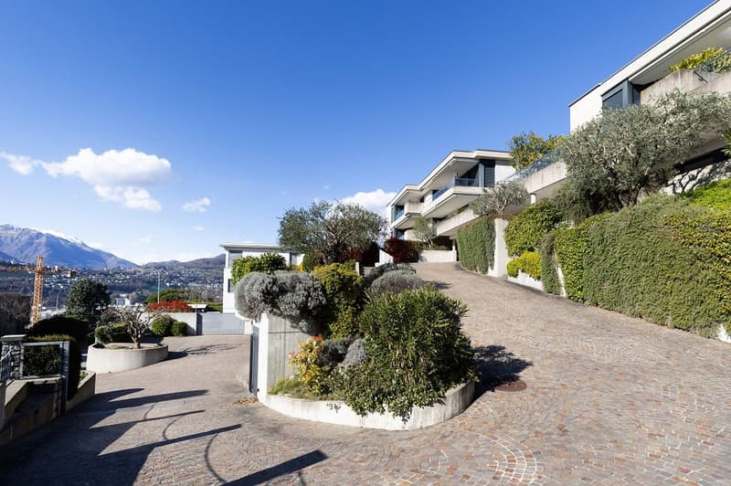 Modern apartment complex with a driveway, surrounded by greenery and mountains in the background