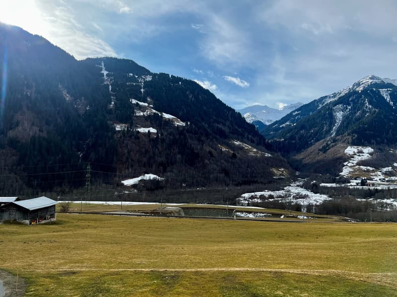 mountain range with snow on peaks, small house, valley, grassland, electric poles, cloudy sky