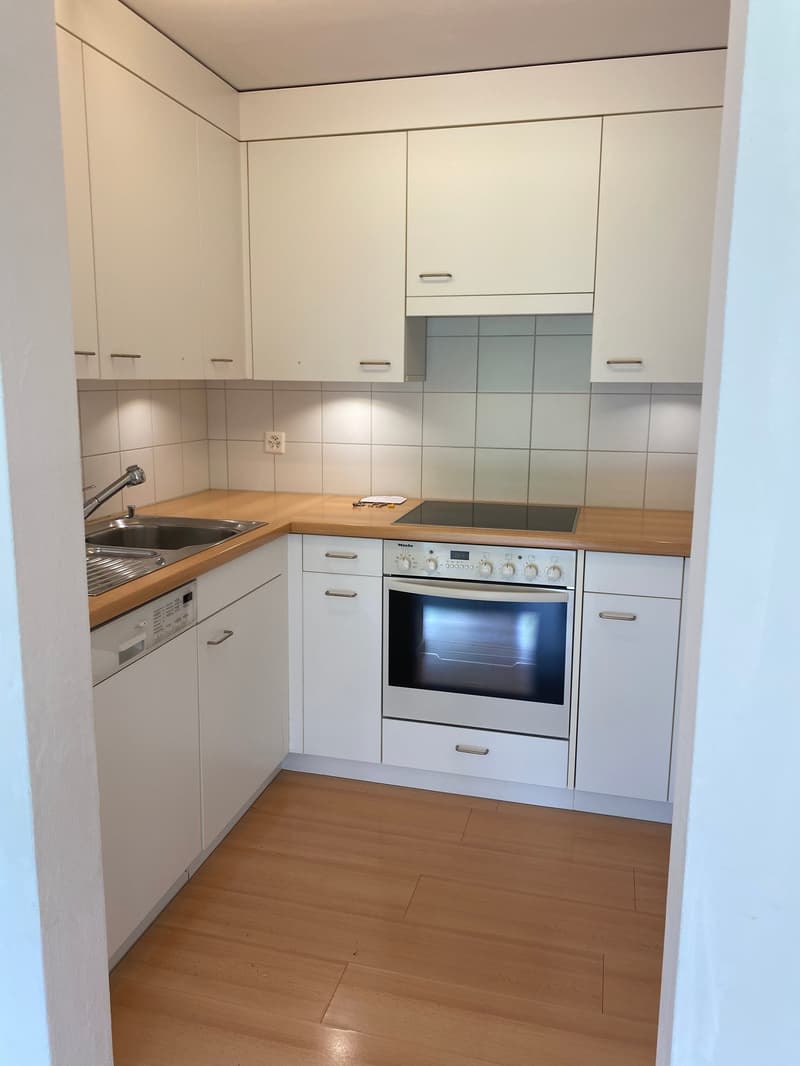 Modern kitchen with white cabinets, wooden countertops, white tiled backsplash, stainless steel sink, dishwasher, gas stove, oven, wooden floors