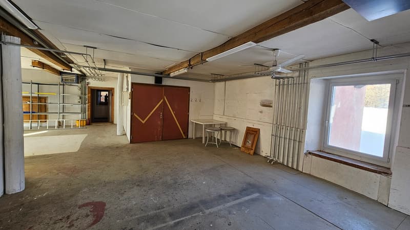 Spacious open room with metal shelves, desk, storage boxes, red double doors, ceiling fan, window with bench seat