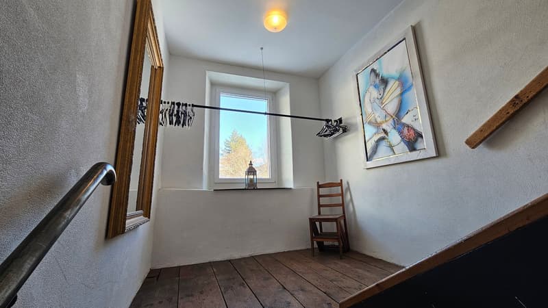 small hallway with a mirror, a picture, a window, a chair, and wooden flooring