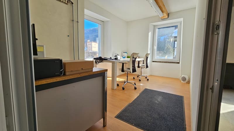 Office room with large windows, desk, two office chairs, monitor, box, printer