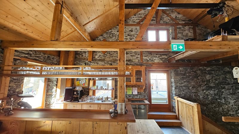 Wooden beam ceiling, stone wall, open kitchen, countertop with cups and bottles, a coffee machine and a sink